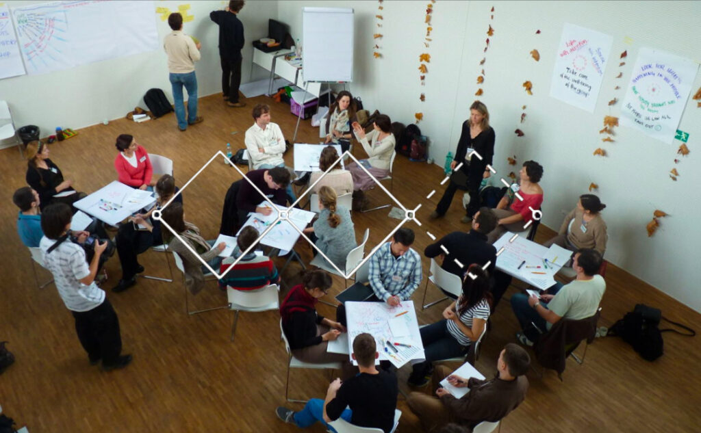 Pessoas reunidas em uma sala, durante dinâmica de design thinking, com diversos post its colados na parede